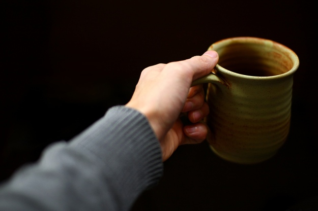 A hand holding the handle of a coffee cup